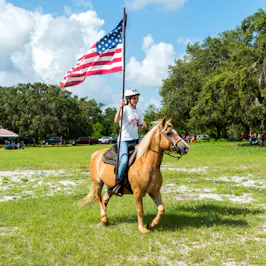 Girl on horseback carrying American flag